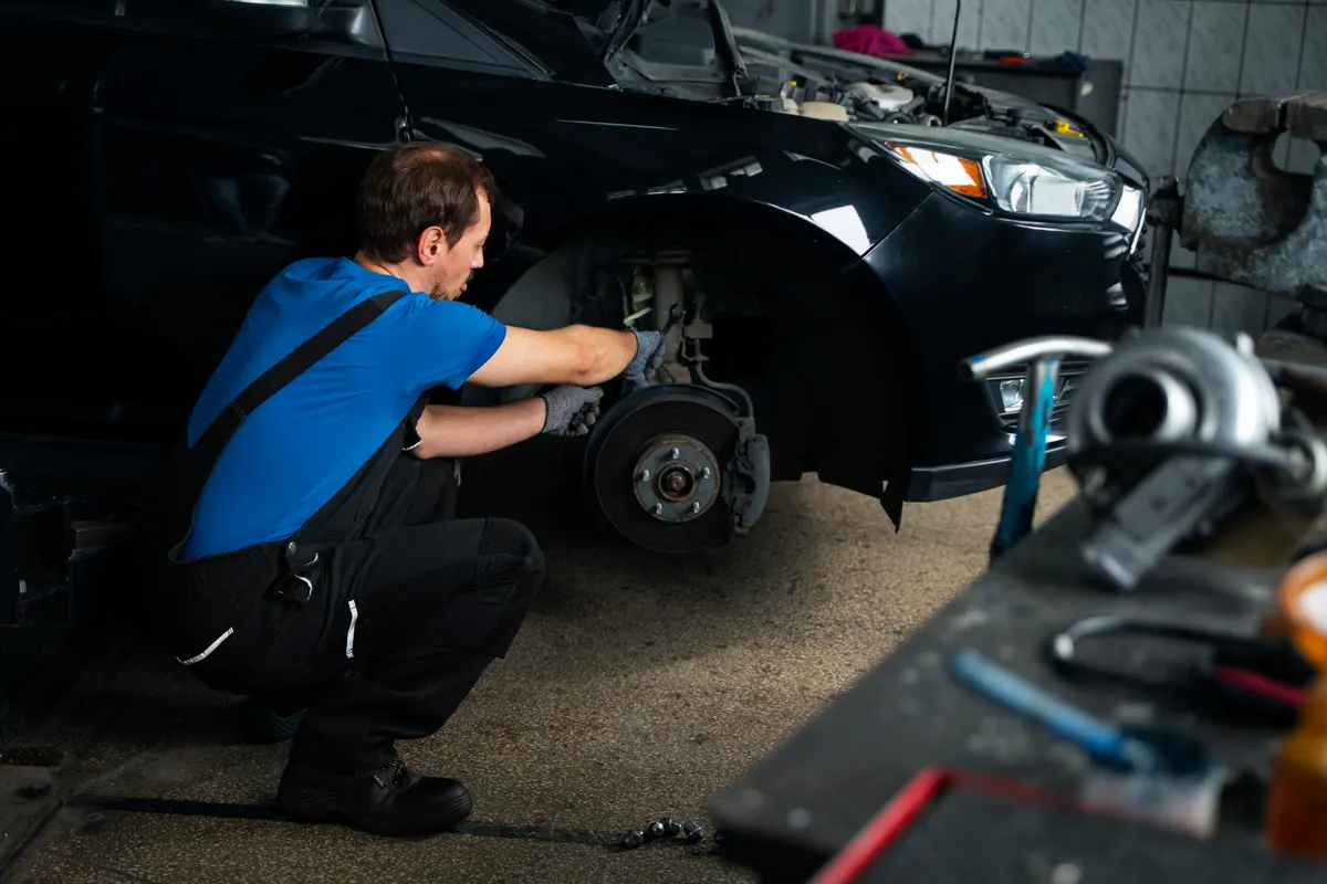 Technician servicing a front brake on a dark car
