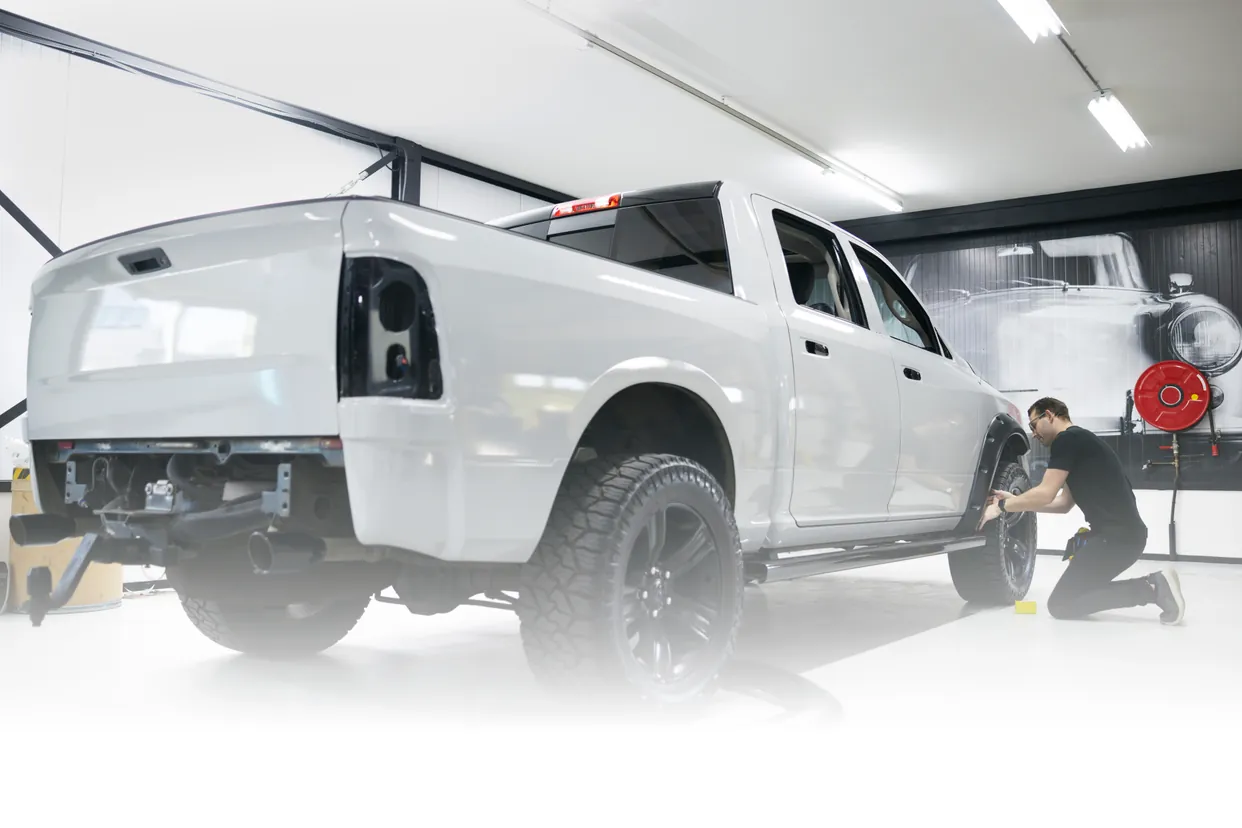 A pickup truck in a clean shop bay while a technician works on its wheel
